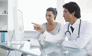 Stock image of a male doctor talking to a female patient while pointing at something on a computer screen