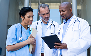 Stock image of three doctors reading off a tablet outside of a hospital building